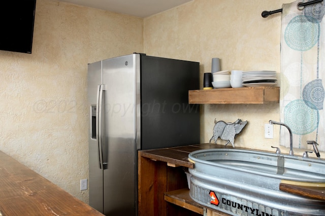 kitchen with a sink, stainless steel refrigerator with ice dispenser, and a textured wall