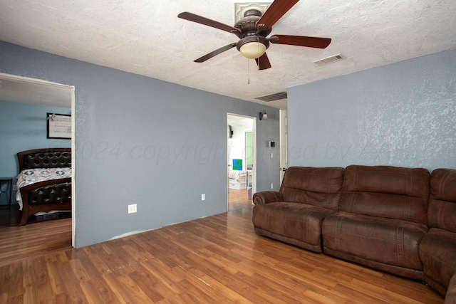 living room with visible vents, a textured ceiling, wood finished floors, and a ceiling fan