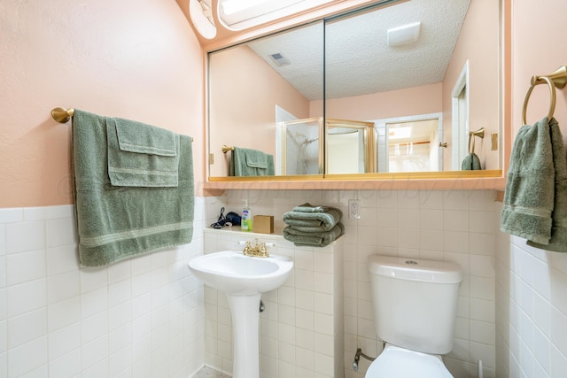 bathroom with a stall shower, visible vents, toilet, a textured ceiling, and tile walls