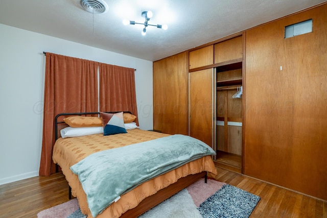 bedroom featuring a closet, visible vents, a textured ceiling, and wood finished floors