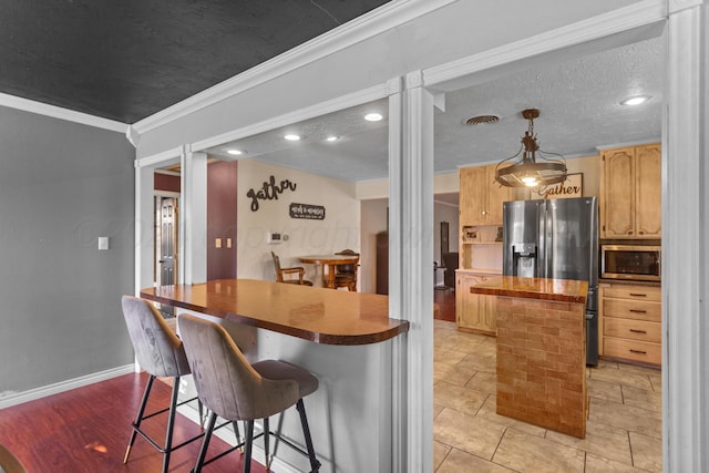 kitchen featuring crown molding, stainless steel appliances, hanging light fixtures, a kitchen breakfast bar, and decorative columns