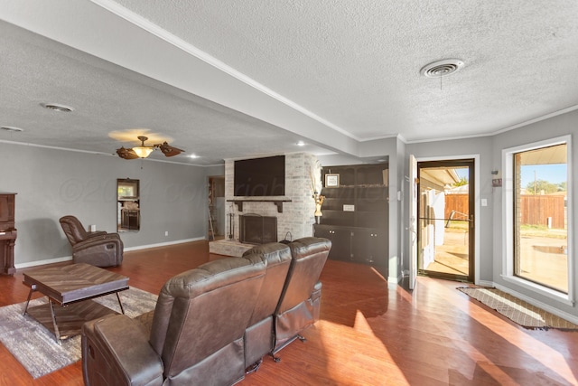 living room featuring a fireplace, wood-type flooring, a textured ceiling, and ornamental molding