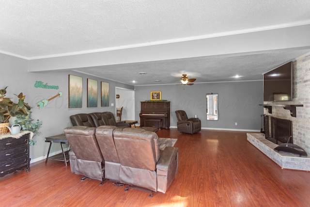 living room with wood-type flooring, crown molding, a textured ceiling, a brick fireplace, and ceiling fan