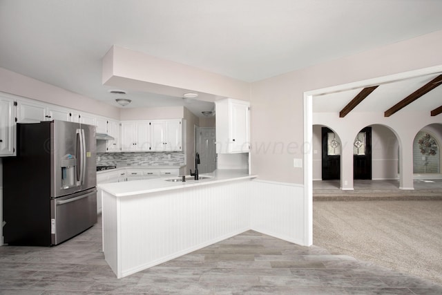 kitchen featuring sink, stainless steel refrigerator with ice dispenser, white cabinets, kitchen peninsula, and beamed ceiling