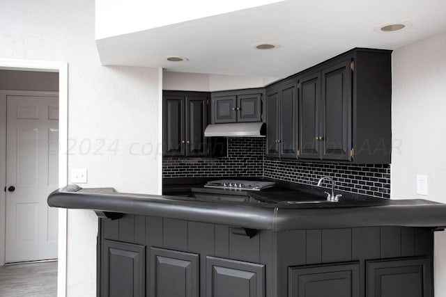 kitchen with sink, kitchen peninsula, hardwood / wood-style flooring, stainless steel gas stovetop, and backsplash