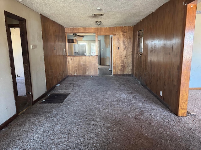 spare room with dark colored carpet, ceiling fan, a textured ceiling, and wooden walls