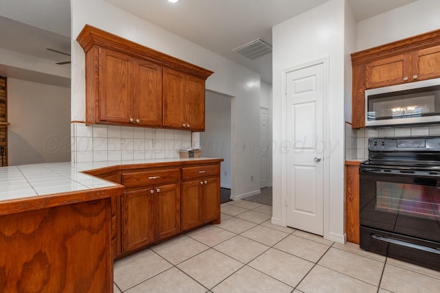 6203 Donda St, Amarillo, TX 79118 - kitchen featuring stainless steel microwave, black / electric stove, brown cabinets, decorative backsplash, and tile countertops