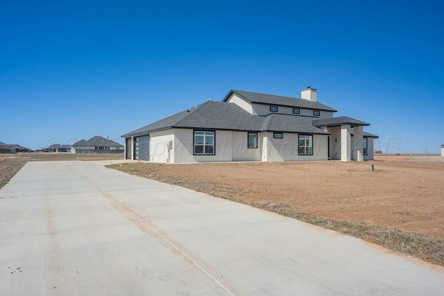 view of front of property with a garage, driveway, a chimney, and a shingled roof