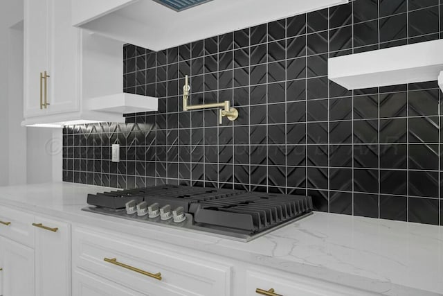 kitchen featuring light stone countertops, stainless steel gas stovetop, white cabinetry, open shelves, and backsplash