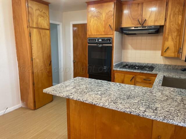 1805 N Jefferson St, Amarillo, TX 79107 - kitchen with under cabinet range hood, brown cabinetry, backsplash, light wood-type flooring, and a peninsula