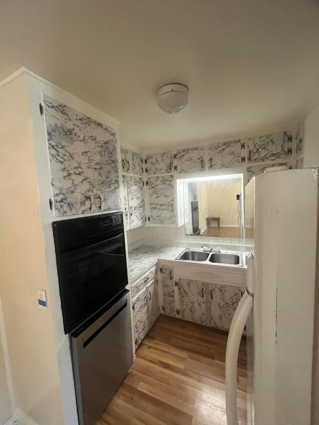 1565 Bell St, Amarillo, TX 79106 - kitchen featuring freestanding refrigerator, black oven, a sink, light wood-style floors, and light countertops