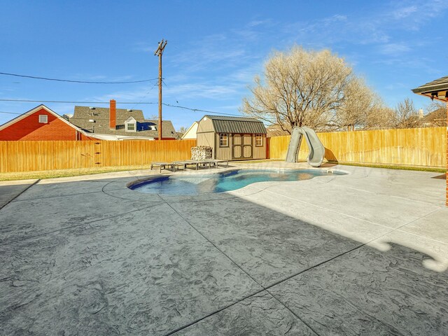 view of swimming pool with a patio area, a fenced backyard, an outbuilding, and a water slide