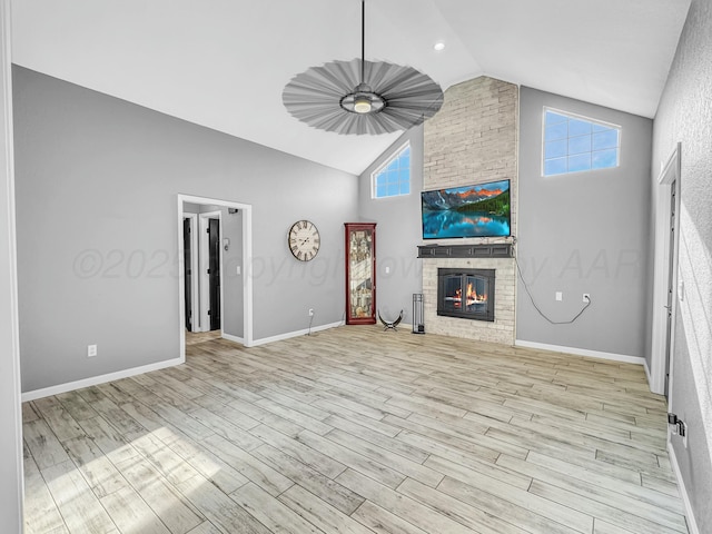 unfurnished living room with a brick fireplace, baseboards, light wood-type flooring, and high vaulted ceiling