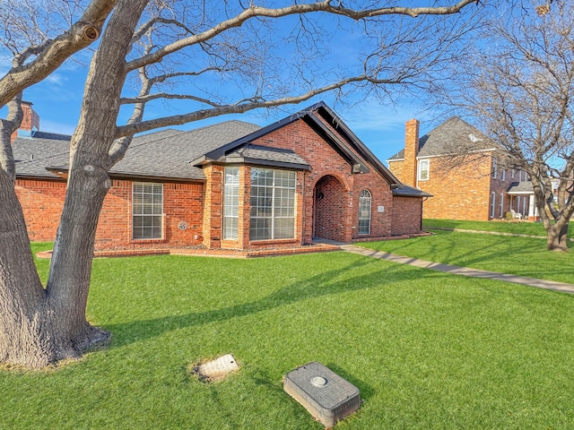 view of front of house featuring brick siding, a front lawn, and roof with shingles