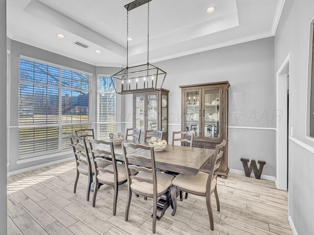 dining space with visible vents, crown molding, light wood-type flooring, and a tray ceiling