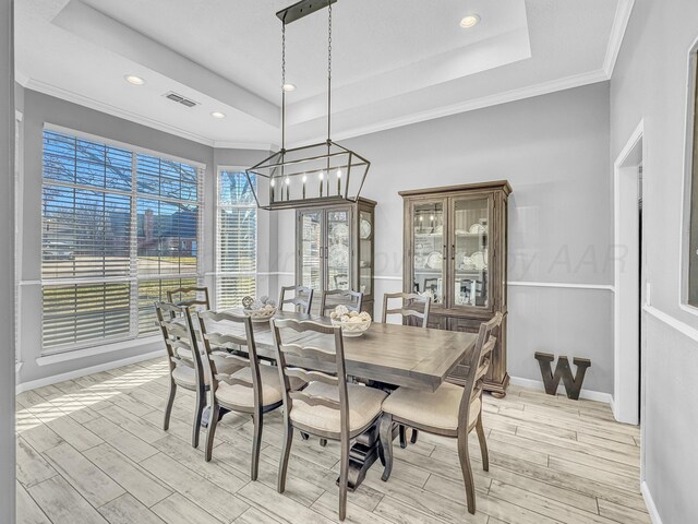 dining space featuring a raised ceiling, light wood-style flooring, and visible vents