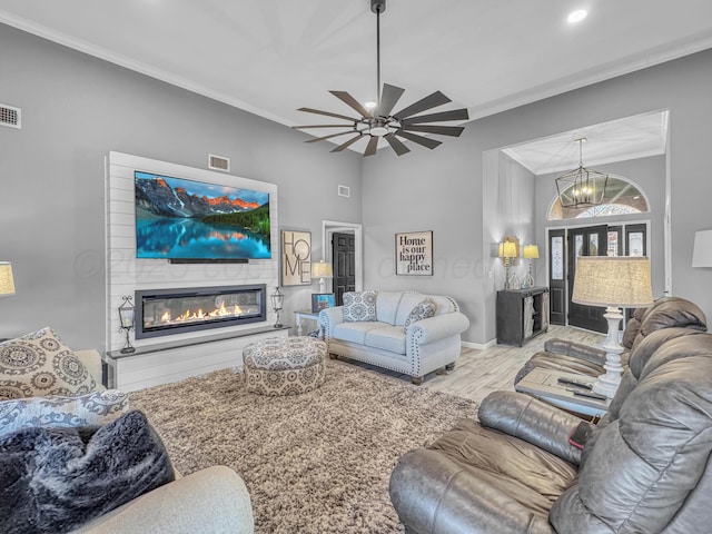 living area with visible vents, wood finished floors, a glass covered fireplace, and crown molding