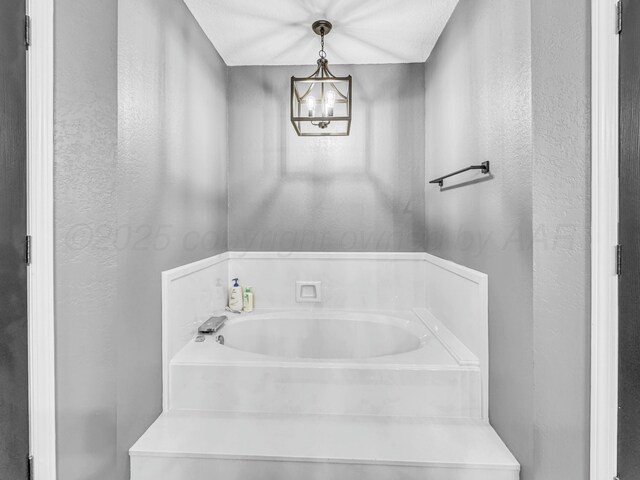 full bath featuring a notable chandelier, a garden tub, and a textured wall