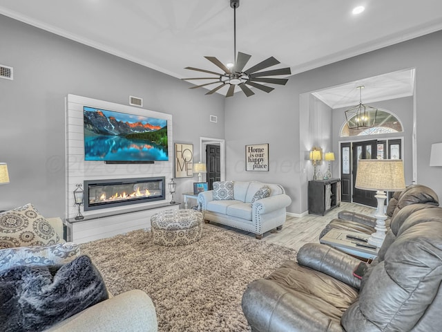 living area with visible vents, wood finished floors, a glass covered fireplace, and ornamental molding