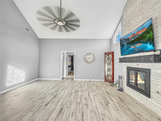 unfurnished living room featuring light wood-type flooring, visible vents, high vaulted ceiling, a fireplace, and baseboards