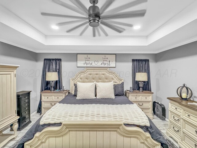 bedroom with baseboards, a tray ceiling, ornamental molding, ceiling fan, and light wood-type flooring