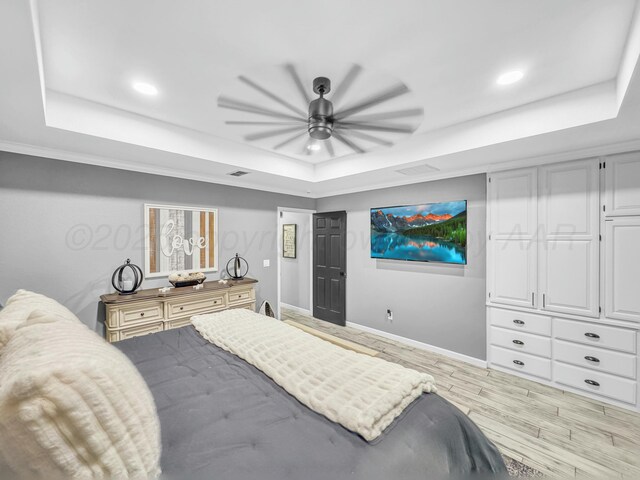 bedroom with a tray ceiling, wood finished floors, baseboards, and visible vents