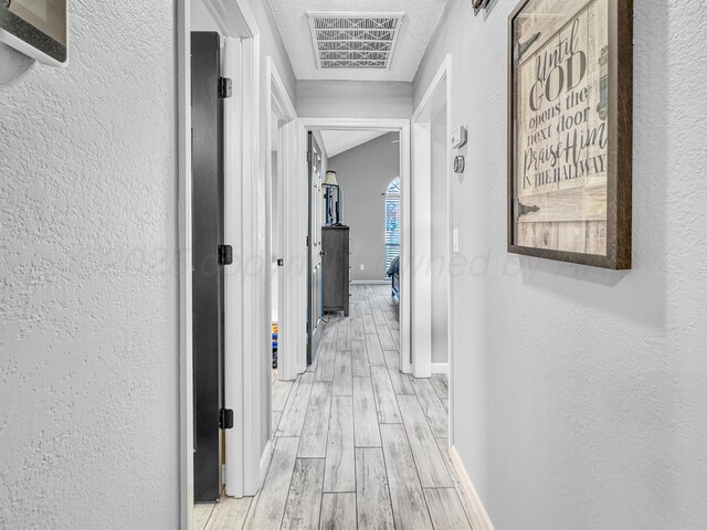 corridor featuring visible vents, light wood-style flooring, baseboards, and a textured wall