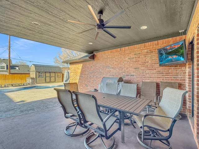 view of patio with an outbuilding, outdoor dining space, a ceiling fan, fence, and a storage shed