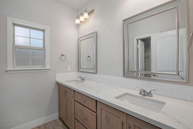 full bathroom featuring double vanity, a sink, baseboards, and wood finished floors