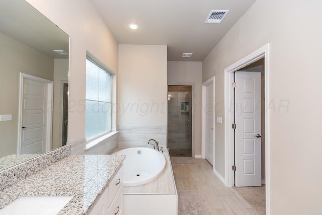 bathroom with a stall shower, a bath, vanity, and wood finished floors