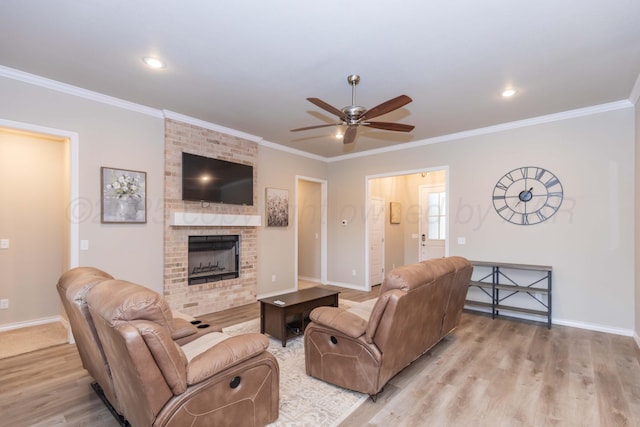 living room featuring ceiling fan, light wood-style floors, baseboards, crown molding, and a fireplace