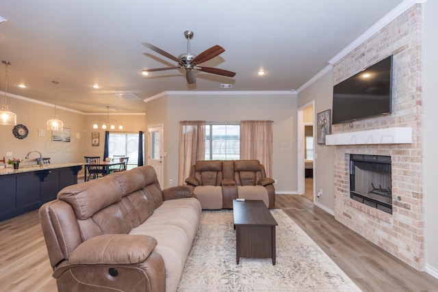 living room with light wood-type flooring, a ceiling fan, ornamental molding, a brick fireplace, and baseboards
