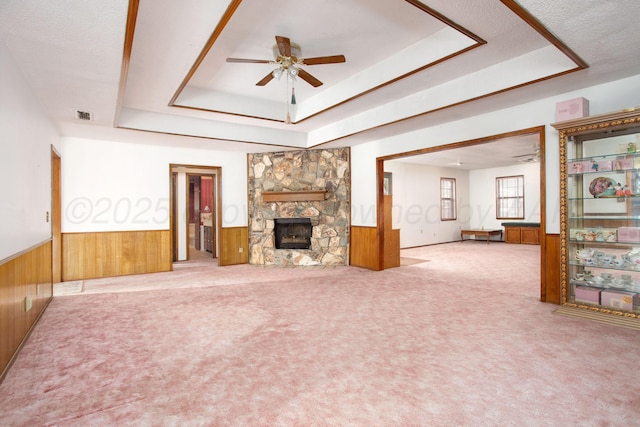 unfurnished living room with a raised ceiling, wooden walls, and wainscoting