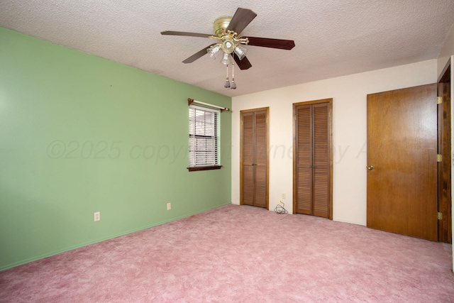 unfurnished bedroom featuring carpet floors, a ceiling fan, two closets, and a textured ceiling