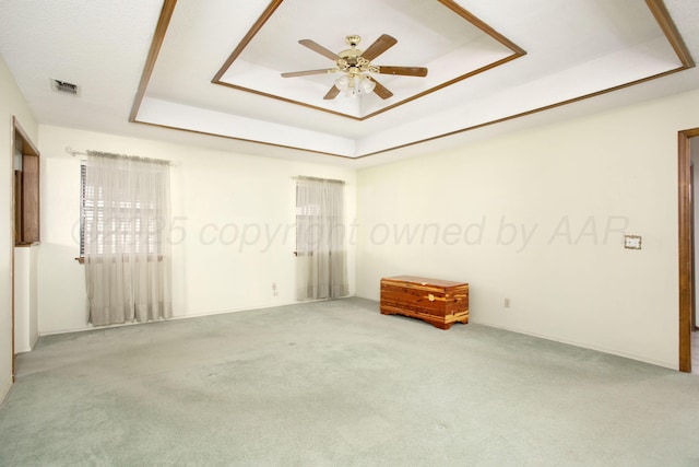 carpeted spare room featuring visible vents, a raised ceiling, and ceiling fan