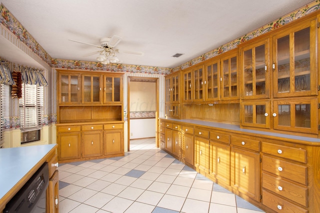 kitchen featuring a ceiling fan, black dishwasher, brown cabinetry, wallpapered walls, and glass insert cabinets