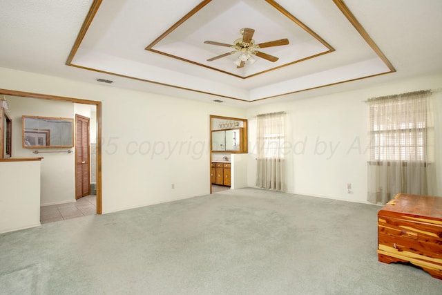 carpeted empty room featuring visible vents, a raised ceiling, and a ceiling fan