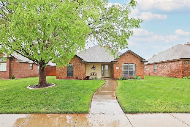 single story home with brick siding, a front yard, and a shingled roof
