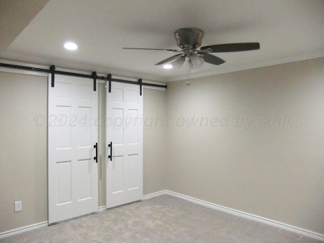 unfurnished bedroom featuring a barn door, ceiling fan, light carpet, and crown molding