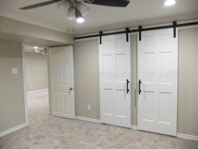 unfurnished bedroom featuring a barn door, light colored carpet, ceiling fan, and crown molding