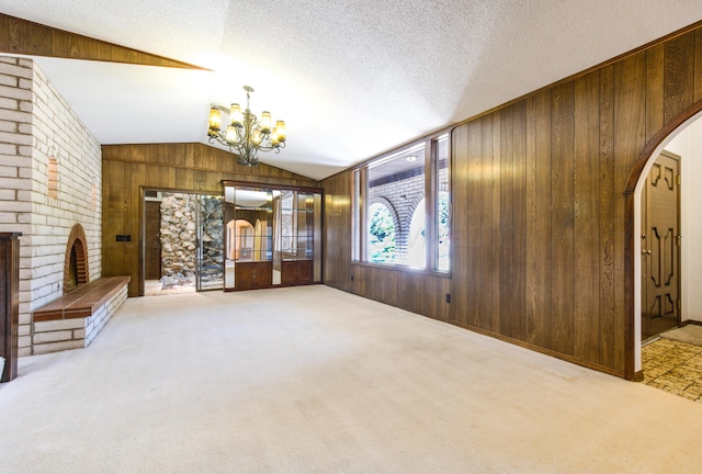 unfurnished living room featuring light carpet, a fireplace, a notable chandelier, and wood walls