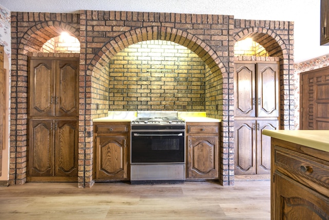 kitchen featuring a textured ceiling, electric range oven, light hardwood / wood-style flooring, and brick wall