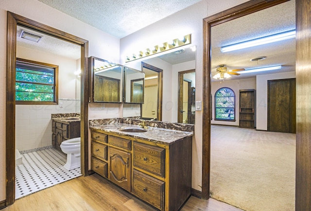 bathroom featuring a textured ceiling, ceiling fan, wood-type flooring, and tile walls