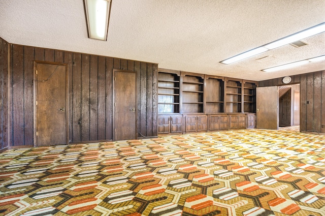 unfurnished living room featuring wood walls, built in features, and a textured ceiling