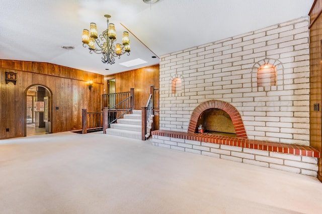 unfurnished living room featuring wood walls, carpet, lofted ceiling with skylight, and a brick fireplace