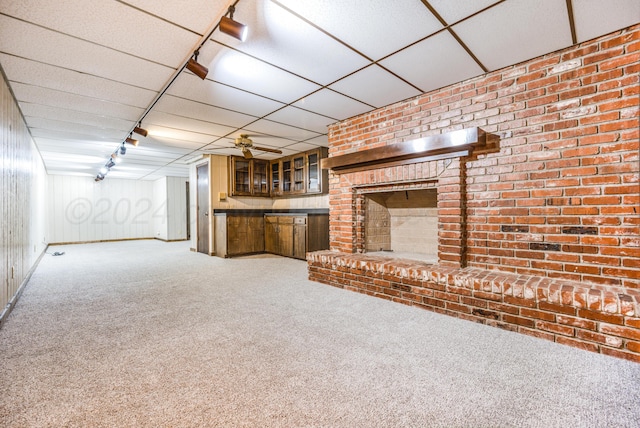 unfurnished living room featuring a drop ceiling, rail lighting, carpet flooring, ceiling fan, and a fireplace