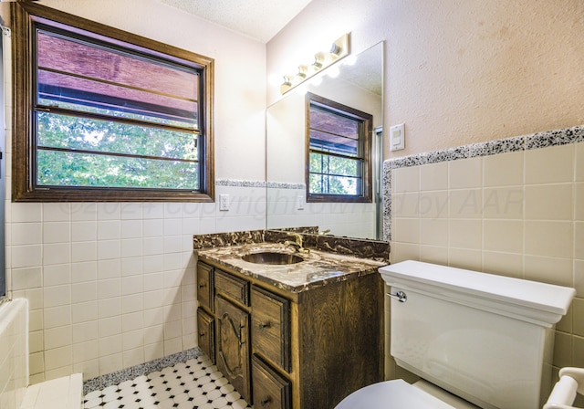 bathroom with a textured ceiling, vanity, tile walls, and tile patterned flooring