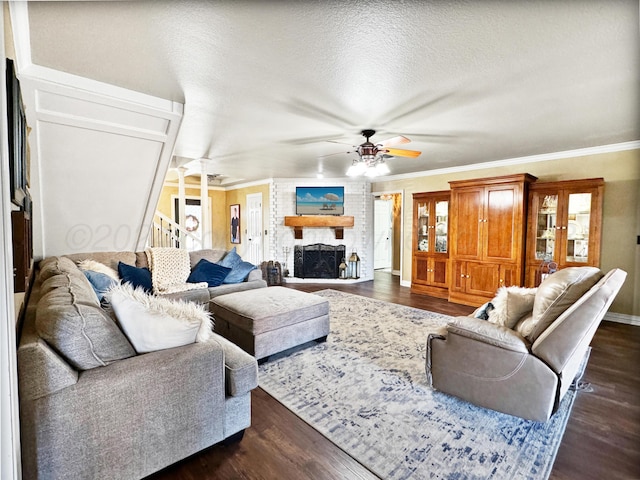 living room featuring ornamental molding, ceiling fan, a brick fireplace, dark wood-type flooring, and a textured ceiling