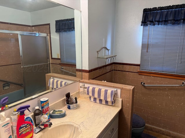 bathroom with vanity, toilet, a shower with shower door, and tile walls