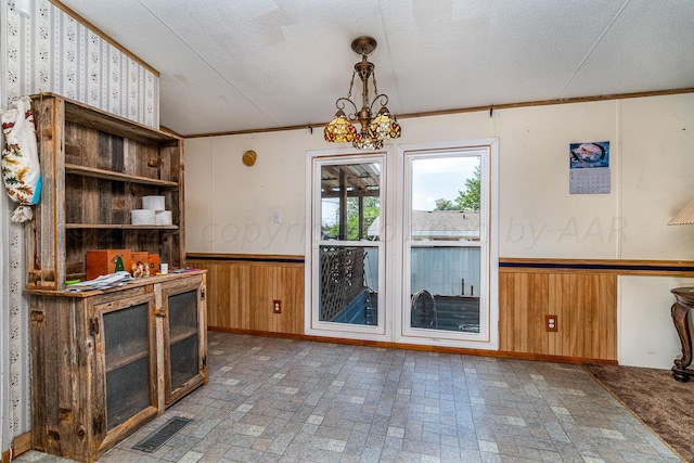 interior space featuring a chandelier, wooden walls, a textured ceiling, and crown molding